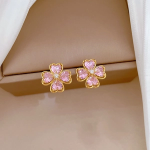 Detailed shot of gold clover stud earrings with pink heart gems on a jewelry box