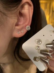 Detail showing three sizes of gold-plated zircon stud earrings on display and worn