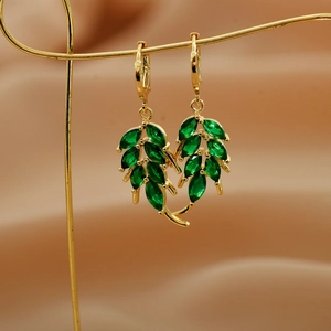 Elegant gold leaf earrings with emerald green gemstones on a soft satin display