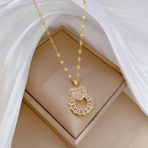 Close-up of golden necklace with crystal heart and ring pendant on beige silk