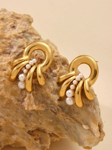 Close-up of gold layered earrings with gradient pearls on textured natural stone base