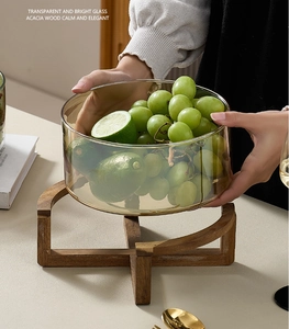 Glass salad bowl with acacia wood base filled with grapes and limes in a home setting