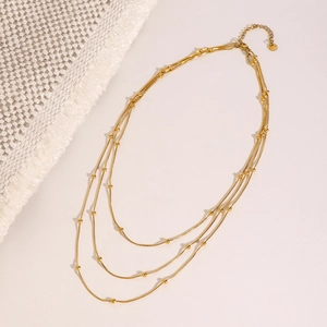 Detailed view of triple-layered gold bead necklace with lobster clasp and extension chain