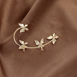 Detailed close-up of gold butterfly ear cuffs with textured wings on brown silk fabric