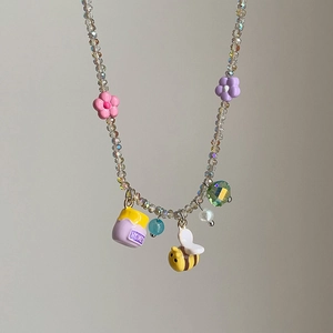 Macro detail of crystal beaded necklace with flower pendants and a honey jar charm