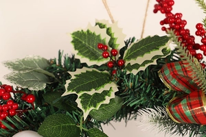 Close-up of artificial pine needles, red berries and plaid bow on Christmas wreath
