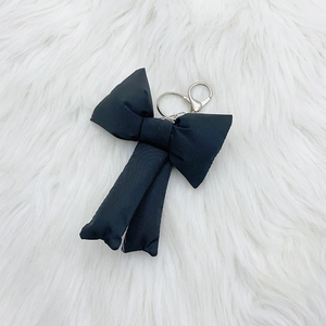Cute black fabric bow keychain with silver metal clasp on soft white plush background