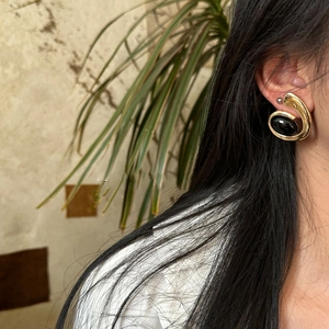 Close-up of elegant gold spiral earrings with black oval stones worn by a model