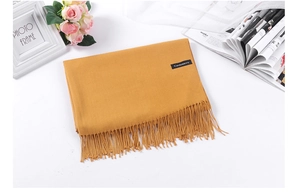 Detailed close-up of a mustard yellow cashmere scarf with fringe edges and brand label