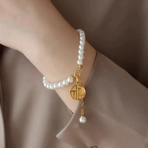 Detailed close-up of 18K gold-plated Fu charm and lustrous pearls on a delicate bracelet