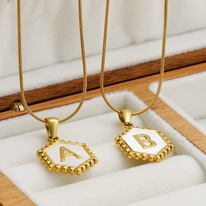 Gold hexagon shell initial necklace with snake chain on white jewelry box
