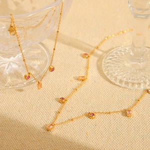 Detail of a gold titanium necklace featuring pink round and square zircon gemstones on linen