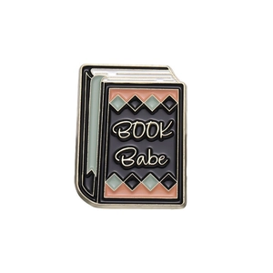Detailed view of an open book enamel pin with 'BOOK Babe' text and geometric patterns