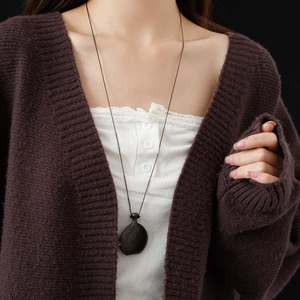 Detail of a dark brown faux wood flask pendant on a pullable sweater chain for women