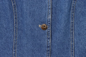 Vue macro détaillée de la texture denim avec surpiqûres orange et bouton en bronze