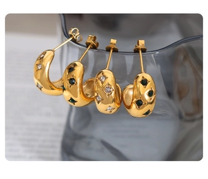 Detailed view of C-shaped gold earrings with zircon starburst settings on a glass rim