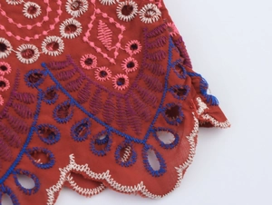 Dettaglio di tessuto rosso ricamato con fiori multicolori e pizzo traforato