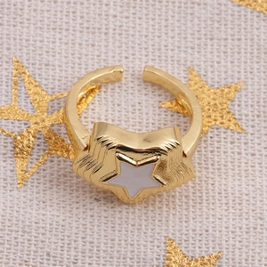 Detailed macro view of a gold-plated star ring with white inlay on a textured beige background