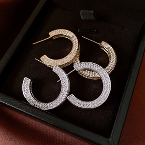 Macro detail of gold and silver C-shaped earrings with micro-pave zirconia on black velvet