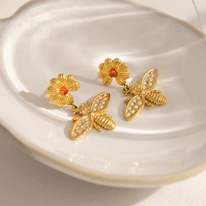 Gros plan détaillé des boucles d'oreilles abeille et marguerite en or 18K et zircons