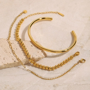Ensemble de trois bijoux en acier doré avec bracelet jonc et chaînes sur socle en pierre
