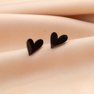 Vue macro de boucles d'oreilles cœur noir minimalistes sur un fond de soie champagne luxueux
