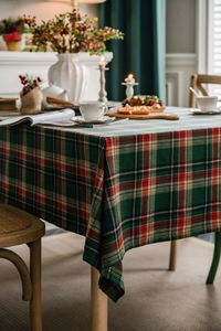 Close-up of green and red plaid tablecloth with festive pine cones and candle setting