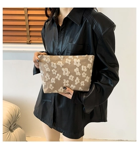 Detail of beige canvas clutch bag with 3D white floral patterns and gold zipper closure
