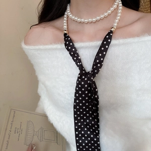 Detail of pearl necklace with polka dot silk scarf on woman wearing white sweater