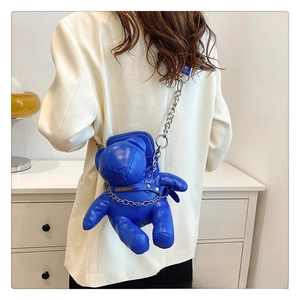 Detail of Klein blue bear-shaped PU crossbody bag with silver chain on white blazer