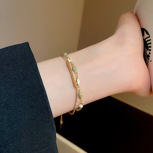 Detail of a double-layered gold plated bracelet with oval enamel beads and geometric pendants