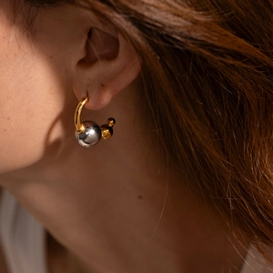 Close-up of gold C-shaped earrings with two-tone silver and gold sphere charms on model