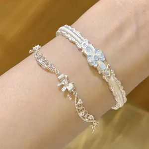 Détails d'un bracelet à nœud argenté et d'un jonc avec fleur bleue sur le poignet