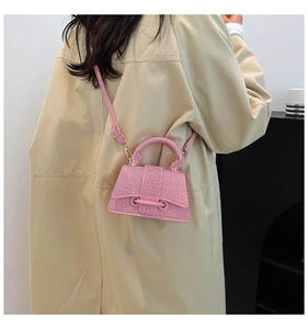 Mini sac bandoulière rose porté par un mannequin avec un trench beige dans un cadre moderne