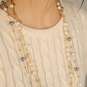 Elegant long necklace with white and grey glass pearls on a soft knit sweater