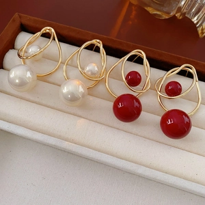 Close-up of gold geometric pearl earrings and red beads in a beige velvet jewelry box