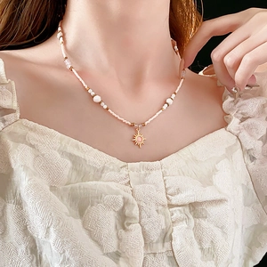 Detail of 18K gold plated sunflower necklace with white beads and pink stone on model