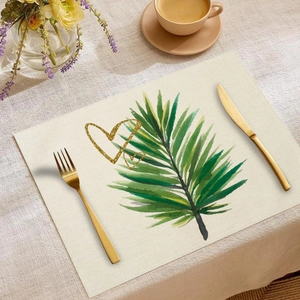 Detail of linen placemat with green palm leaves and golden heart print on dining table
