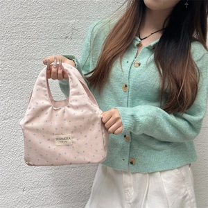Detail of floral pink lunch bag with brand tag held by hand against a white wall