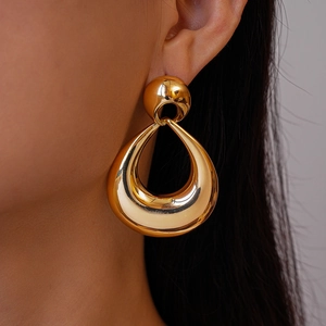 Close-up of a large gold hollow water drop earring worn by a model in a vintage metal style