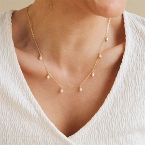 Close-up of minimalist gold chain necklace with cascading oval pearls on a model neck