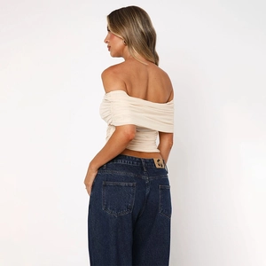 Detail of off-shoulder pleated mesh top in beige and high waist wide leg blue jeans