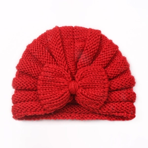 Detail view of soft red knitted infant hat with large bow and intricate knit texture