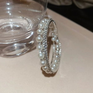 Detailed view of elegant double-layer pearl and rhinestone bracelet near a glass cup