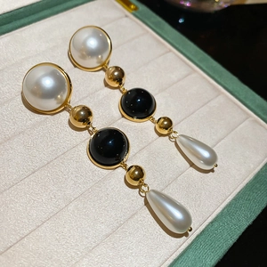 Macro detail of 18k gold plated drop earrings with white pearls and black enamel beads