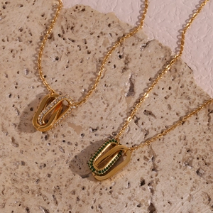 Close-up of interlocking gold pendant necklace with green gemstone and white zircon accents