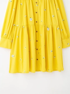 Close-up of white floral embroidery and brown buttons on yellow cotton linen dress