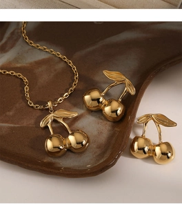 Golden cherry jewelry set with necklace and earrings on a brown ceramic plate