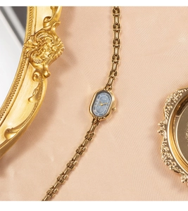 Detail of elegant gold ladies' watch with dark oval dial on beige silk background