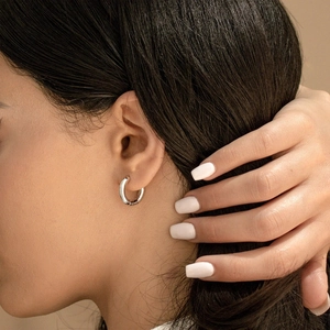 Close-up of polished silver stainless steel hoop earring on model with mirror finish
